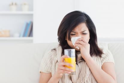 sick woman blowing her nose holding a glass of orange juice