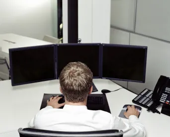 professional man about to start a video call facing three monitors at his work desk