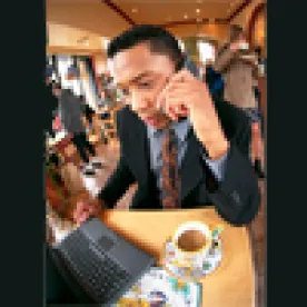 man working in a coffee shop with his laptop and on a call 