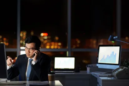 professional man on his cell phone at work late at night with three computers in a city hi rise 