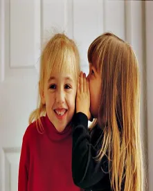 A little girl whispering into another girl's ear
